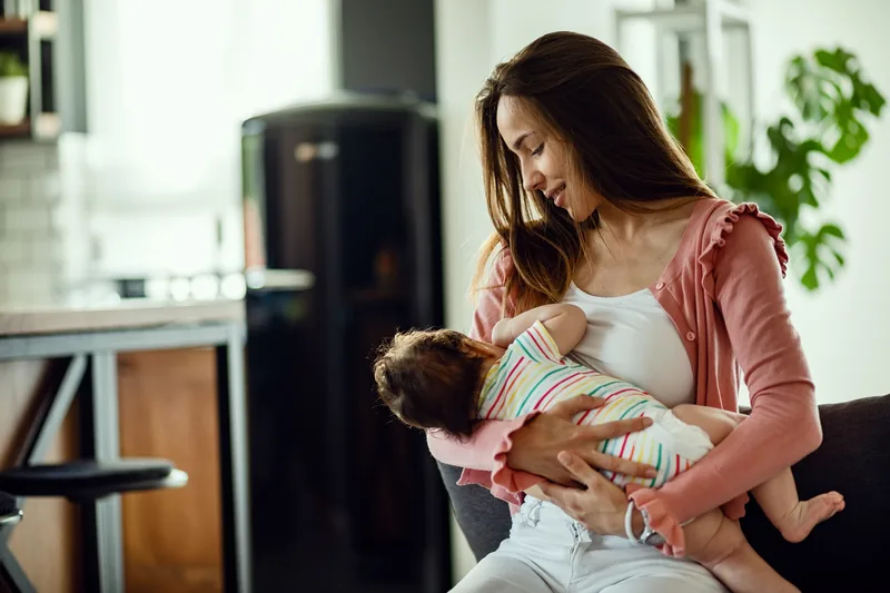 Maman souriante allaitant son bébé à la maison